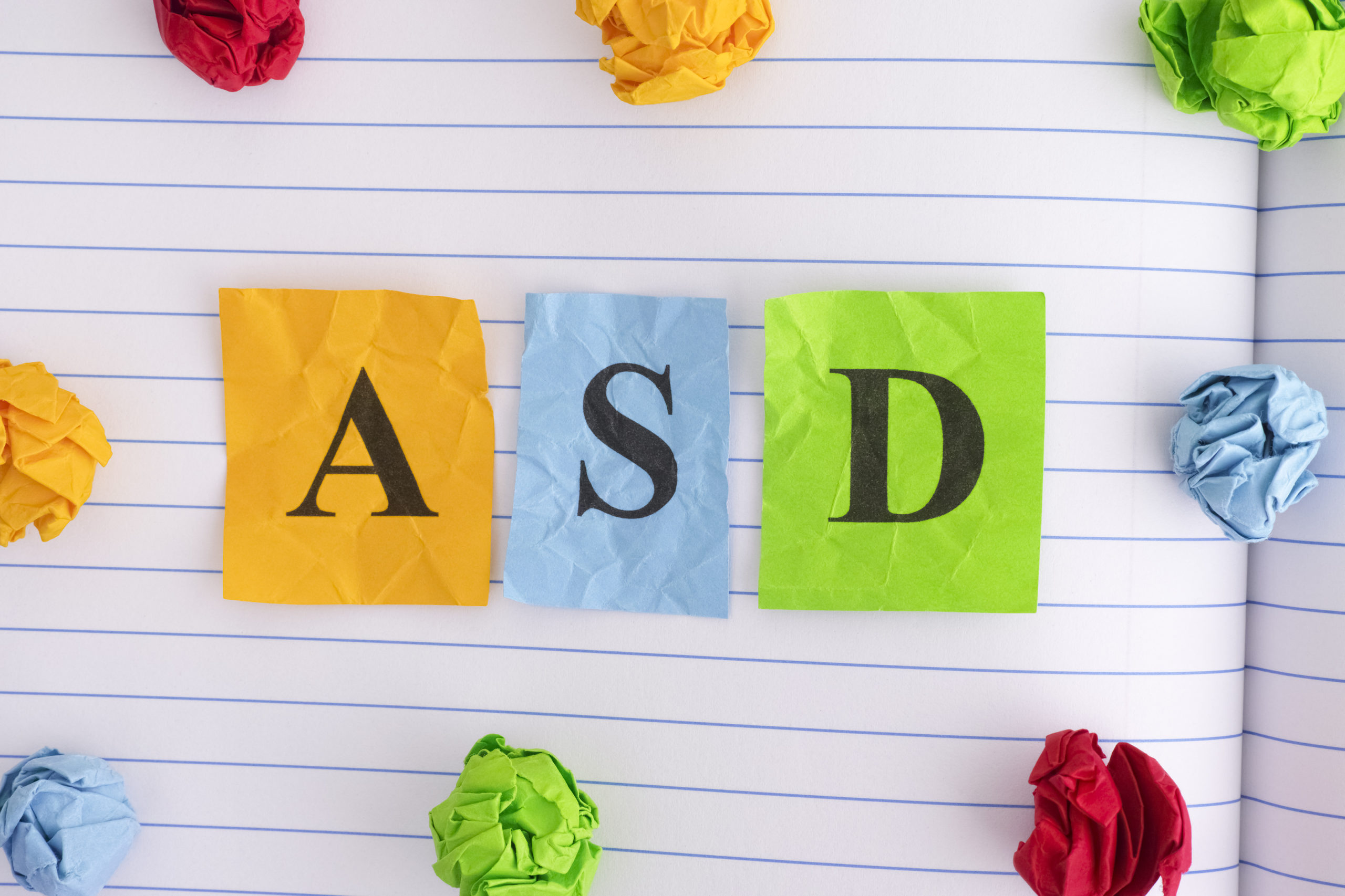 ASD. ASD (Autism spectrum disorder) on notebook sheet with some colorful crumpled paper balls around it. Close up.