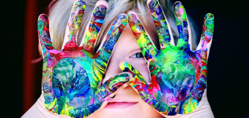 A child with autism spectrum disorder peeks out from behind colorfully painted hands.